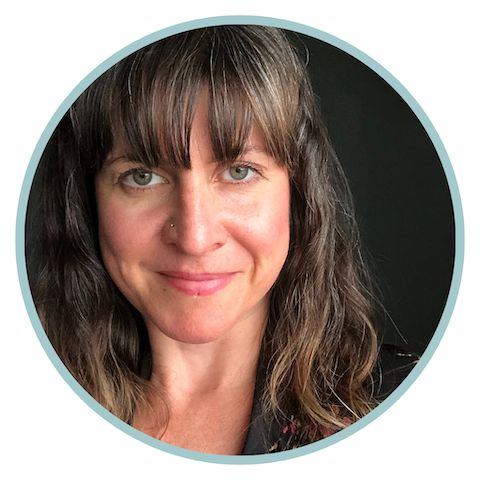 Image of Emily Pike, Certified Life and Leadership Coach - A woman with long, wavy brown hair and bangs is smiling softly in this headshot. She has light skin and green eyes, and she is wearing a nose stud. The background is dark, which highlights her features. The image is enclosed within a circular border.